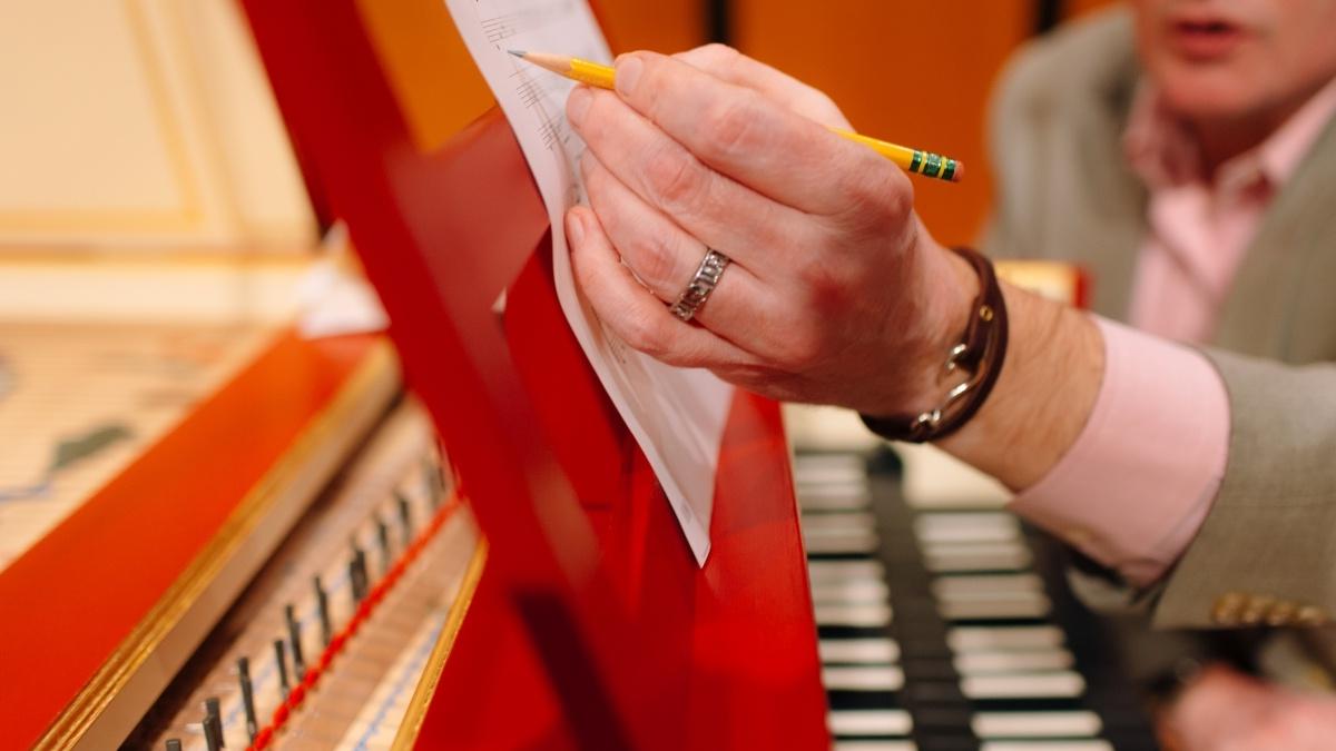 Person marking sheet of music while on harpsichord